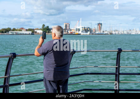 A middle aged man taking a picture at the seaside using his mobile phone or cell phone Stock Photo