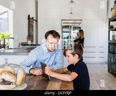 Father and son using digital tablet at dining table Stock Photo