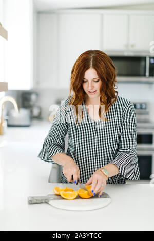 Woman slicing orange in kitchen Stock Photo