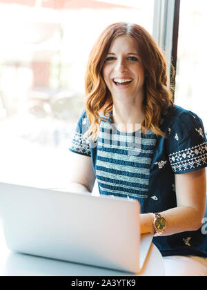 Smiling woman using laptop in cafe Stock Photo