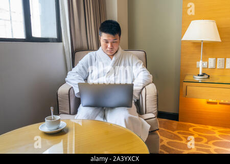 Asian man using laptop and having coffee at hotel room Stock Photo