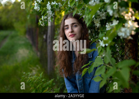 Young woman wearing denim jacket by white flowers Stock Photo
