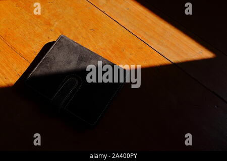Closeup of a closed black book placed on wooden table under sunlight, black book concept Stock Photo