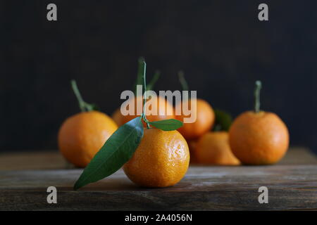 Close up of single fresh mandarin with leaf and many mandarins blurry on wooden table Stock Photo