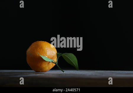 Close up of single fresh mandarin with leaf on wooden table Stock Photo