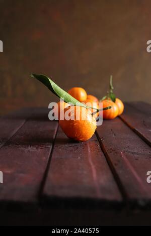 Close up of single fresh mandarin with leaf and many mandarins blurry on wooden table Stock Photo