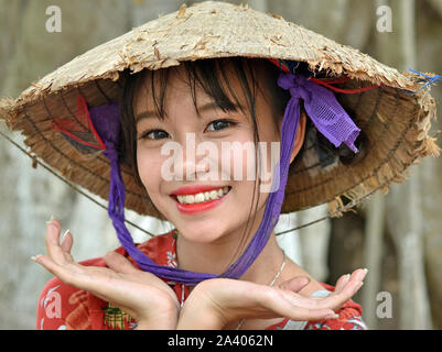 Young Vietnamese woman wears an old Asian conical hat (rice hat) and poses for the camera. Stock Photo