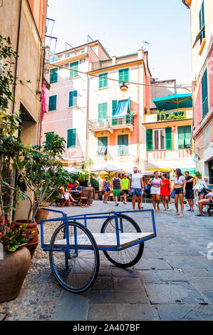 Monterosso Al Mare, Italy - September 02, 2019: Blue cart with two wheels standing on a cozy street full of vibrant buildings, walking people, shops a Stock Photo