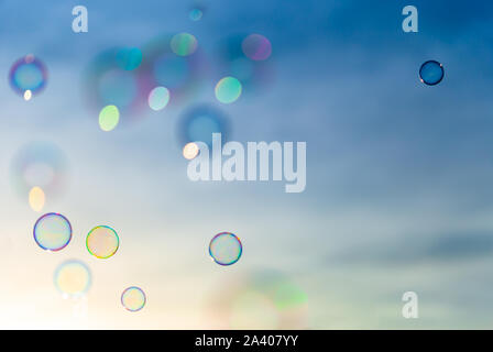 Colorful soap bubblesflying towards a blue and orange sky while the sun is setting. Stock Photo