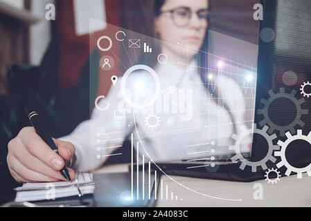Confident businesswoman working on laptop and notepad at her workplace at modern office. Concept of virtual diagram,graph interfaces,digital display,c Stock Photo