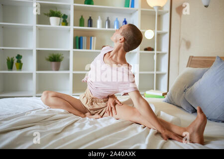 Charming and smilng fitness woman in pajamas doing exercises at home on bed. Healthy lifestyle concept Stock Photo