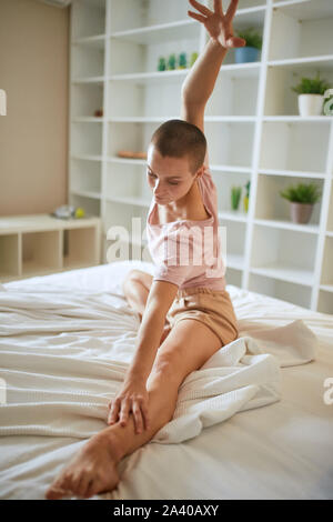 Charming and smilng fitness woman in pajamas doing exercises at home on bed. Healthy lifestyle concept Stock Photo