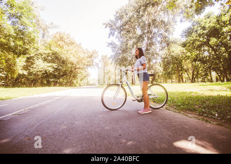 Young sporty woman with the bicycle, wearing jeans shorts, enjoy a summer day in nature. Stock Photo