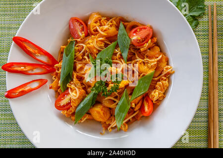Thai traditional noodle dish Pad Thai with chicken served on white ceramic plate. Top view. Chopsticks on the side. Green background. Stock Photo
