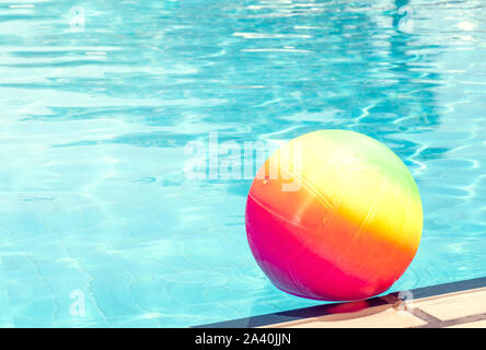 Bright rainbow ball in a swimming pool turquoise water. Concept of a joyful summer vacation. Idea of outdoor games in the summertime. Copy space for t Stock Photo