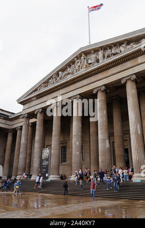 The facade and forecourt of the British Museum in London, United Kingdom. Visitors leave and enter the main entrance on a rainy summer's day. Stock Photo