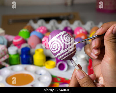 Coloring eggs with various colors beautifully with the brush during the Easter. Woman paint on easter eggs. Beautiful art on eggs in easter festival. Stock Photo