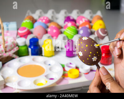 Coloring eggs with various colors beautifully with the brush during the Easter. Woman paint on easter eggs. Beautiful art on eggs in easter festival. Stock Photo