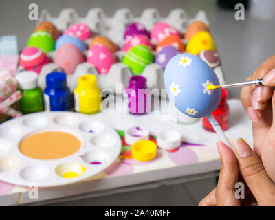 Coloring eggs with various colors beautifully with the brush during the Easter. Woman paint on easter eggs. Beautiful art on eggs in easter festival. Stock Photo