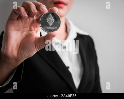 Businesswoman showing silver ethereum coin on the white wall is background. Investors woman holding silver ethereum coin from mined in the Internet. Stock Photo