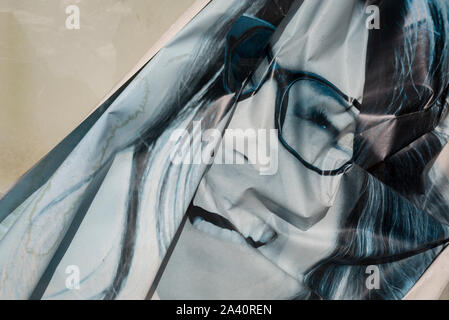 A detail of a crumpled advertising poster in a display window featuring a smiling model wearing glasses, on 2nd October 2019, in Sutton, London, England Stock Photo