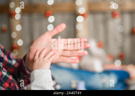 baby's hand holds mother's hand. against the background of a defocus of new year's garlands. Christmas little miracle. new year, christmas, new year Stock Photo