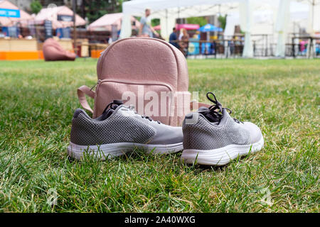 Pink leather female backpack and gray sneakers on a green lawn in the park. The concept of outdoor recreation, hiking in the summer season. Stock Photo