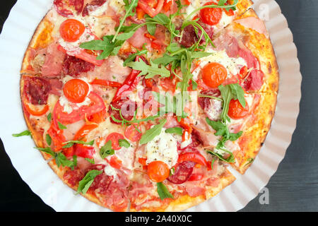 Pizza with cherry tomatoes, bacon, mozzarella and arugula top view. Round thin-crust pizza with vegetables and meat. Stock Photo