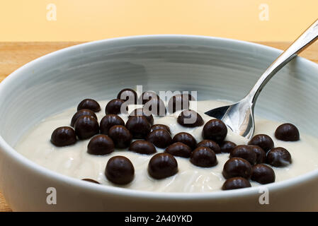 Hazelnut yogurt with chocolate crispies in a white cup on wooden table. Stock Photo