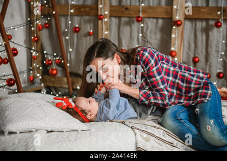 baby and mom on christmas background. happy family mom and child little daughter son and christmas miracle. gently playing with your baby on the bed Stock Photo