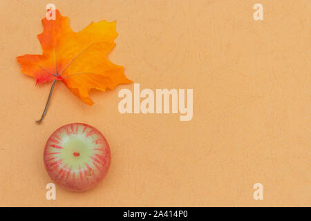 Warm fall seasonal orange  flatlay with festive maple leaf and small ornamental red apple on open concept and copy space availability. Stock Photo