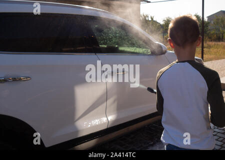 A middle-aged man teaches children of boys 4 and 10 years old to wash a car in the yard of his house on a summer sunny day. 2019.09.22. Odessa. Ukrain Stock Photo