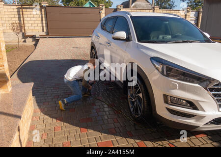 A middle-aged man teaches children of boys 4 and 10 years old to wash a car in the yard of his house on a summer sunny day. 2019.09.22. Odessa. Ukrain Stock Photo