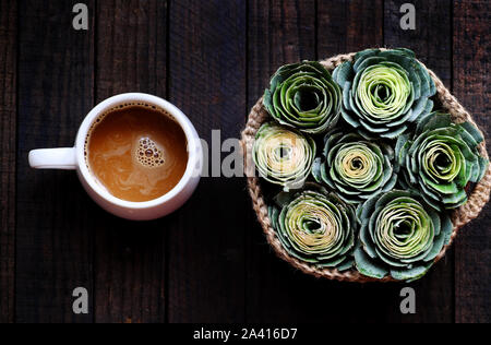 Top view white coffee cup with basket of green rose for morning coffee time at home on black wooden background Stock Photo