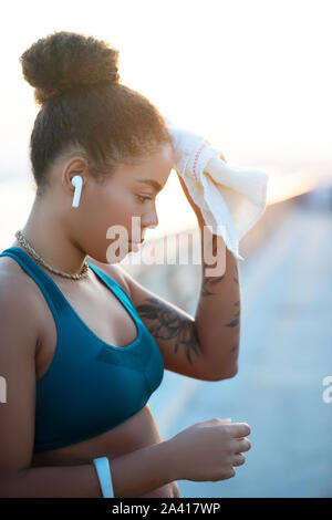 Dark-haired woman with tattoo on arm drying sweat on forehead Stock Photo