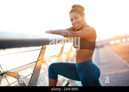 Dark-eyed young woman with tattoo on arm stretching after run Stock Photo