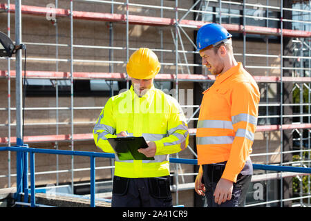 A Male Supervisor Looking At Architect Writing On Clipboard Standing At Construction Site Stock Photo