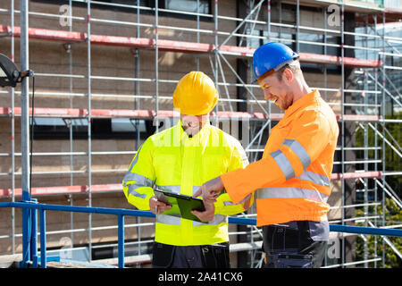 A Male Supervisor Looking At Architect Writing On Clipboard Standing At Construction Site Stock Photo