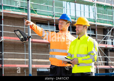 A Male Supervisor Looking At Architect Writing On Clipboard Standing At Construction Site Stock Photo