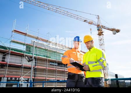 Rear View Of Two Male Architect Wearing Hardhat Looking At Construction Site Stock Photo