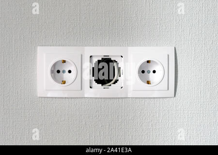 Three sockets located under the TV on the wall. The middle outlet is still in the installation process. Stock Photo
