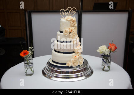 Four tiered wedding cake with icing sugar flowers all down the one side decorating it, cream flowers made of icing, navy ribbon around the tiers Stock Photo