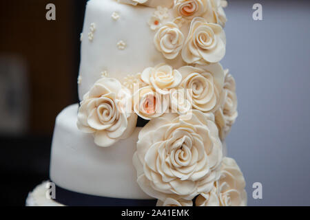 Four tiered wedding cake with icing sugar flowers all down the one side decorating it, cream flowers made of icing, navy ribbon around the tiers Stock Photo