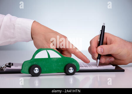 Close-up Of Man's Hand Signing Sales Contract For Car At Dealership Against Gray Background Stock Photo