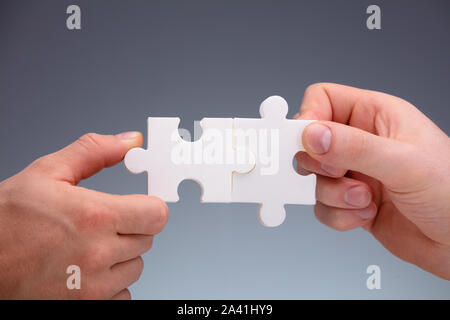 Close-up Of Two People's Hand Joining White The Jigsaw Puzzles Pieces On Gray Background Stock Photo