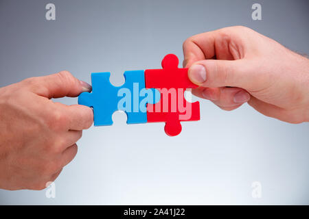 Close-up Of Two People's Hand Joining White The Jigsaw Puzzles Pieces On Gray Background Stock Photo