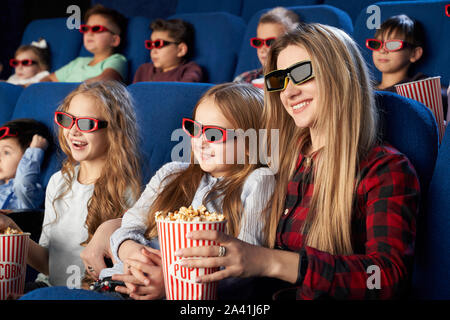 Happy mother and daughter wearing 3d glasses and eating tasty popcorn in cinema. Cheerful family watching funny film and enjoying spare time together in movie house. Concept of enjoyment and fun. Stock Photo