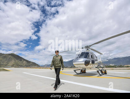 (191011) -- LHASA, Oct. 11, 2019 (Xinhua) -- Jianre Yixi walks before a helicopter in southwest China's Tibet Autonomous Region, Aug. 7, 2019. The Qinghai-Tibet Plateau was once known as a 'no-fly zone' and it was extremely difficult to fly helicopters there. Now, after professional and intensive training, the first batch of young Tibetans has flown civilian helicopters to the Mt. Qomolangma base camp.     Jianre Yixi is from an impoverished herdsman family in Damxung County, Tibet. In 2016, Jianre Yixi, a student at Lhasa's No. 2 Secondary Vocational and Technical School, received a call to c Stock Photo