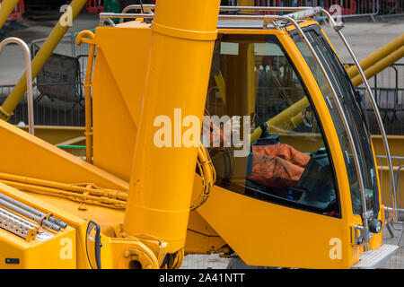 Building site machinery digger driver with feet up sitting in cab at controls of big earth mover digger. Stock Photo