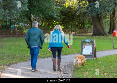 a trendy middle aged couple walking a dog in the countryside in the grounds of holkham hall in Norfolk. Stock Photo